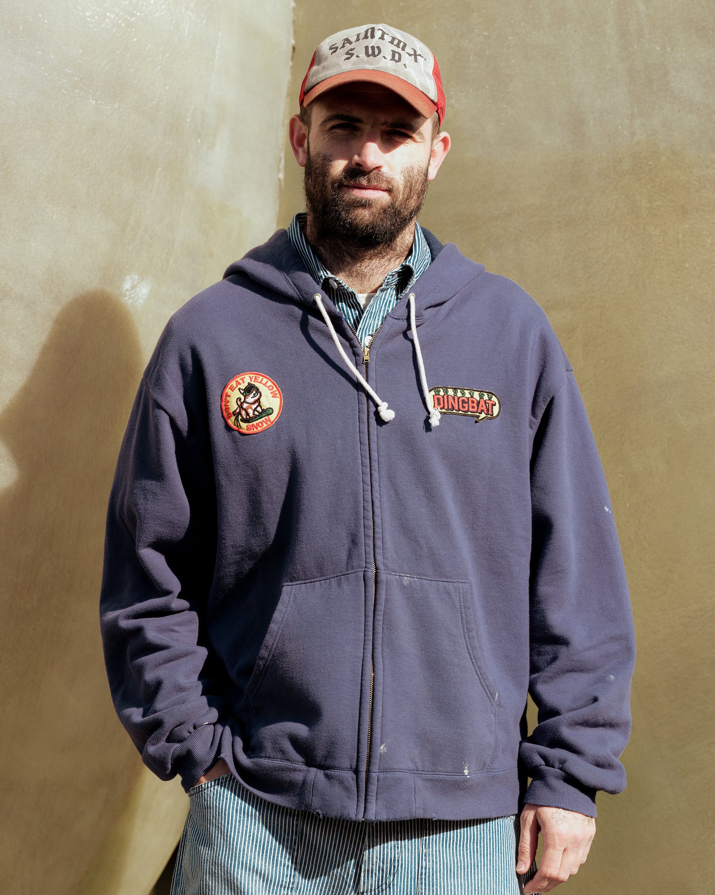 SWJP Zip Hoodie - Sean Wotherspoon Designs 公式。ワッペン付きネイビーフーディーを着た男性、屋外でポーズ。